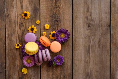 Renkli Macarons ve ahşap masa arka plan üzerinde çiçekler. Fransız tatlı taze çiçekler ile. Üstten Görünüm. Sonbahar konsepti