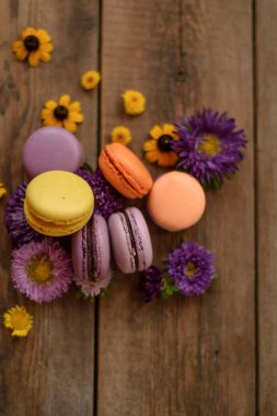 Renkli Macarons ve ahşap masa arka plan üzerinde çiçekler. Fransız tatlı taze çiçekler ile. Üstten Görünüm. Sonbahar konsepti