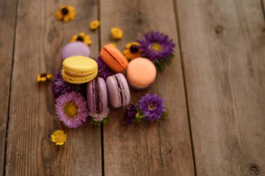Mor ve sarı macarons ve ahşap masa arka plan üzerinde çiçekler. Renkli Fransız tatlı taze çiçekler ile