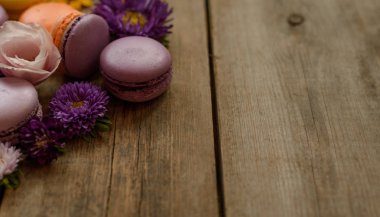 Mor ve sarı macarons ve ahşap masa arka plan üzerinde çiçekler. Renkli Fransız tatlı taze çiçekler ile