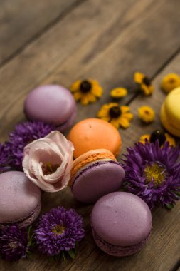 Mor ve sarı macarons ve ahşap masa arka plan üzerinde çiçekler. Renkli Fransız tatlı taze çiçekler ile.