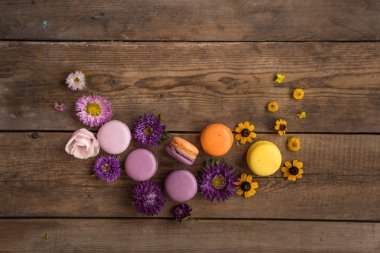 Macarons ve ahşap bir tablonun arka planını çiçekler. Renkli Fransız tatlı taze çiçekler ile. Mor ve sarı arasında degrade. Metin için yer
