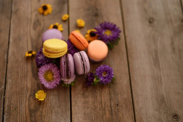 Mor ve sarı macarons ve ahşap masa arka plan üzerinde çiçekler. Renkli Fransız tatlı taze çiçekler ile