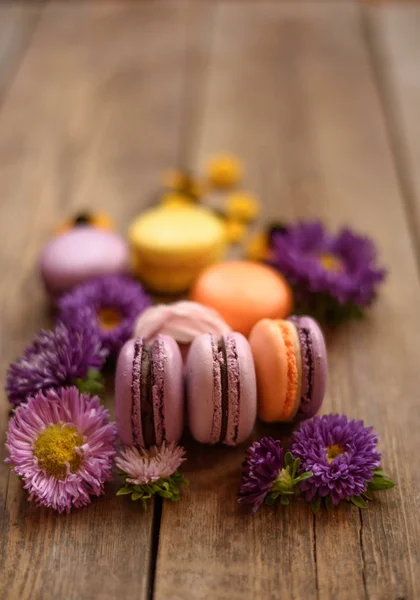 Mor ve sarı macarons ve ahşap masa arka plan üzerinde çiçekler. Renkli Fransız tatlı taze çiçekler ile.