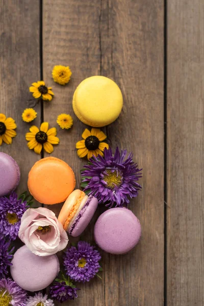 Renkli Macarons ve ahşap masa arka plan üzerinde çiçekler. Fransız tatlı taze çiçekler ile. Üstten Görünüm