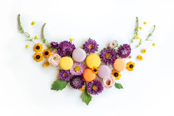 Wieniec Macarons i kwiaty na białym tle. Kolorowy deser francuski ze świeżymi kwiatami. Widok z góry — Zdjęcie stockowe