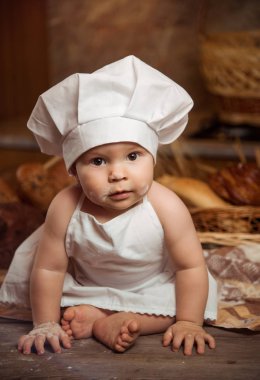 Mutlu küçük çocuk aşçı kostüm ile lezzetli rulo, ekmeği ve ekmek sepetleri arasında masadaki oturan mutfak at. Kopya alanı.