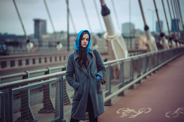 Young woman in the coat, walks on the city bridge during the windy weather. Urban autumn winter style