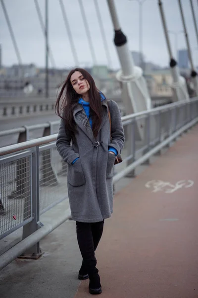 Young woman in the coat, walks on the city bridge during the windy weather. Urban autumn winter style