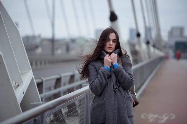 穿着大衣的年轻女子 在刮风的天气里走在城市的桥上 城市秋天冬天样式 — 图库照片