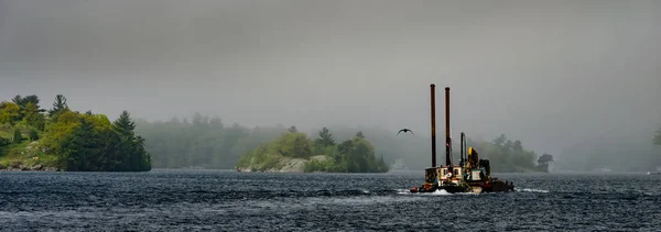 Panorama of Tugboat and barge on a river passing three fog shrou