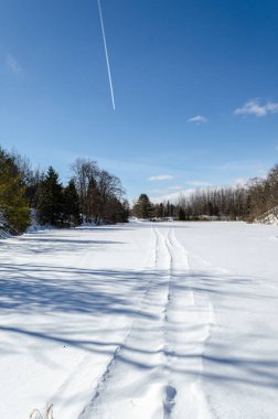 Donmuş gölet, jet izlerinin altında kar motosikleti izleri var.