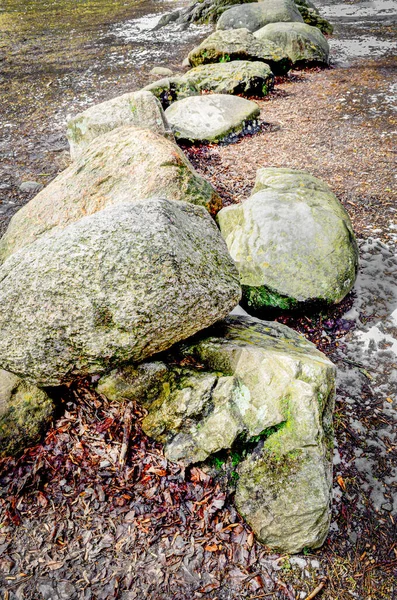 Close-up of a row of stones next to light snow in a field