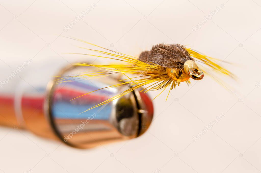 Macro front view of a single yellow fishing fly in a vise against a white background
