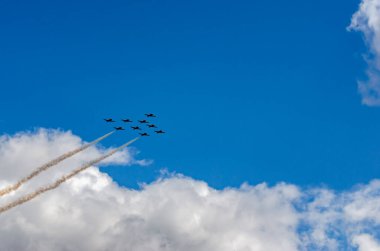 Siluetli dokuz jet savaşçısı bulutlu mavi gökyüzüne karşı buhar izleri oluşturdu.