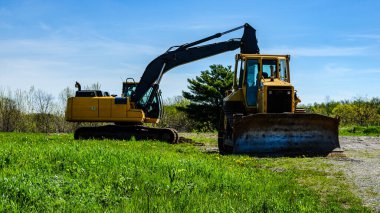 Kazıcı ve buldozer güneşli bir günde çakıllı bir yolun yanındaki tarlada..