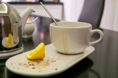 Çaydan sonra lekeli kirli fincan ve tatlının geri kalanı bir tabakta, siyah yemek masasında bir dilim limon standı, yumuşak bir odak