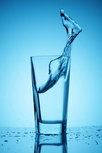 Salpicos de bebida limpa e água doce em uma xícara de vidro em um fundo azul clássico — Fotografia de Stock