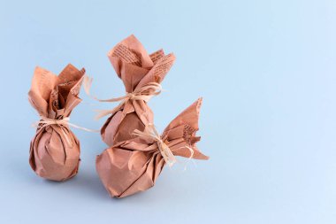Mavi arka planda kahverengi kraft kağıdına sarılı Paskalya yumurtaları. Yeşil tüketimin kavramsal görüntüsü.