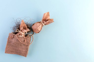 Çuval bezinin düz paskalya düzeni, mavi arka planda el işi kağıdında yumurtalar. Çevre dostu minimalist hediye tüketimi kavramı. Boşluğu kopyala
