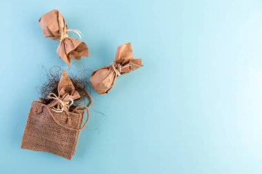 Paskalya yumurtaları, çevre dostu el sanatları kağıdına sarılıp mavi arka planda doğal bir kırsal çuval bezinden yapılmış bir hediye çantasına konmuş. Düz yerde, üst tarafta. Boşluğu kopyala.