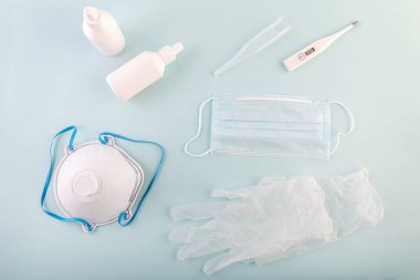 Coronavirus salgını COVID-19. Virüslere karşı korunmak için antiviral tıbbi maske, tıbbi solunum cihazı, termometre, mavi arka planda dezenfektan. Karantina, evde kal..