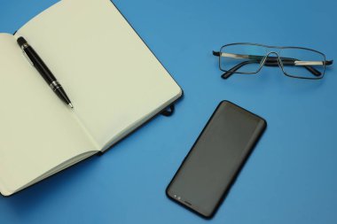 dizüstü bilgisayar, akıllı telefon, mavi arka planda kalem ve gözlük