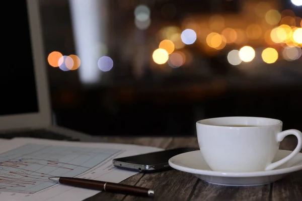 work from home, a cup of coffee and a laptop on a night background with beautiful bokeh