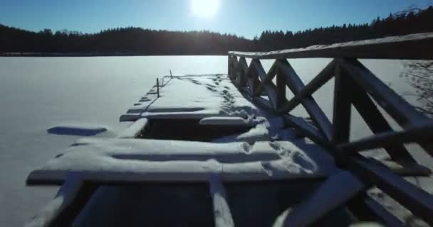 空中。美しい日当たりの良い冬の非常に寒い日にリトアニアで凍った湖の上ショットをお披露目。木造の橋の滑らかな離陸は。4 k — ストック動画