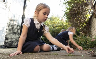 Okul üniforması giyen küçük bir kız. Düşüncelere dalmış bahçede oynuyor.. 