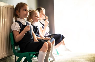 Okul üniforması giymiş üç kız sandalyede oturup yemek yiyor.