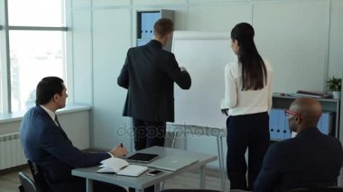 Ben başka bir Suggestion/In büyük pencereler ekibi ile geniş ofis var mali rapor anlatılmaktadır. Tablet, dizüstü bilgisayar ve kalem masanın üzerinde. Onlar iş takım elbiseli giyindin. Onlara, büyük pencereler, dolaplar klasörlerle, bir flipchart