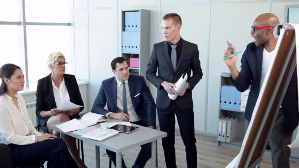 Un homme d'affaires a trouvé une solution logistique intéressante / Dans le bureau spacieux avec de grandes fenêtres équipe discute du rapport financier. La tablette, l'ordinateur portable et les stylos sur la table. Ils sont habillés en costume d'affaires. Derrière eux, grandes fenêtres, armoires avec 