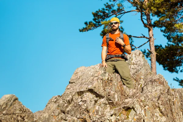 Young male with beard is traveling through the mountain, tourist rucksack standing on rock hill while enjoying nature view, summer holidays in mountains — Stock Photo, Image