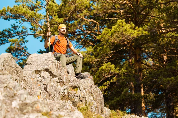 Young male with beard is traveling through the mountain, tourist rucksack standing on rock hill while enjoying nature view, summer holidays in mountains — Stock Photo, Image