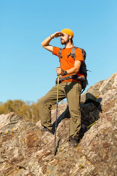 Young male with beard is traveling through the mountain, tourist rucksack standing on rock hill while enjoying nature view, summer holidays in mountains — Stock Photo, Image