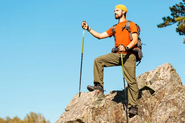 Young male with beard is traveling through the mountain, tourist rucksack standing on rock hill while enjoying nature view, summer holidays in mountains — Stock Photo, Image