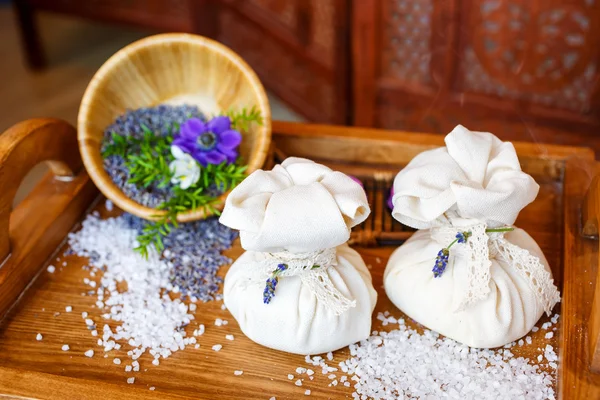 Bodegón, bolsas de sal para masajes, con flores, sobre hierbas en el spa . — Foto de Stock