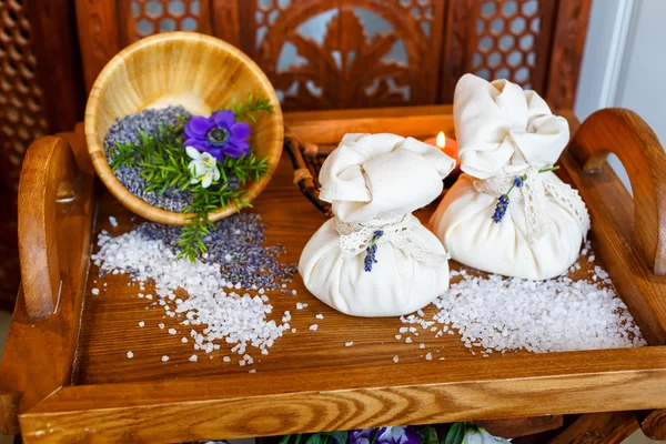 Bodegón, bolsas de sal para masajes, con flores, sobre hierbas en el spa . — Foto de Stock