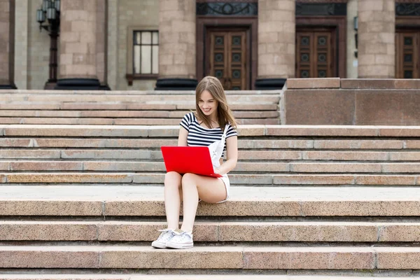 Mladá krásná žena s laptopem sedí na schodech nedaleko univerzity — Stock fotografie
