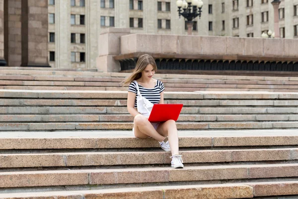 Young beautiful woman with laptop sitting on stairs near the university — Stock Photo, Image