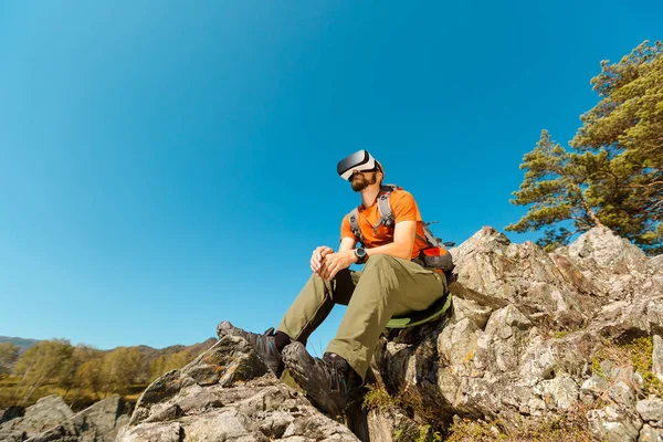 Successful young man, using virtual reality goggles to tour in mountains, on vacation in summer — Stock Photo, Image