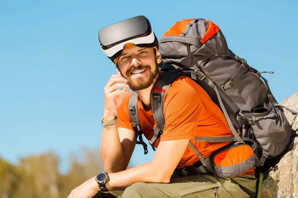 Successful young man, using virtual reality goggles to tour in mountains, on vacation in summer