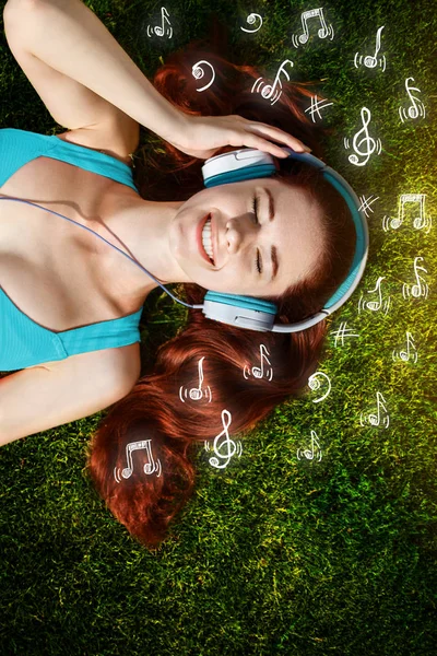 Młoda kobieta z słuchawki na zielonej trawie w parku, muzyka, infografika — Zdjęcie stockowe