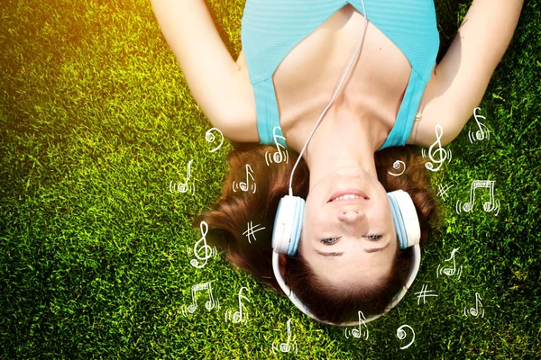 Jeune femme avec écouteurs sur herbe verte dans le parc, musique, infographie — Photo