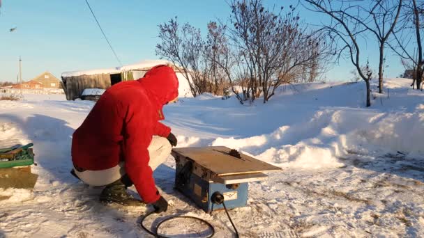 Joven reparando, sierra circular, invierno en la calle, en el campo — Vídeos de Stock