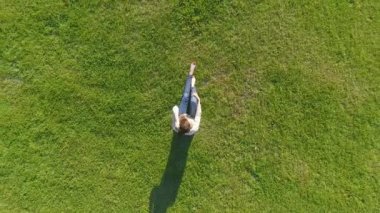 Havadan görünümü. Genç kız yalan ve bahçede çimlerin üzerine park güneşli günde dinlenme. Görünümünün üzerinde. Kadın çayır çim üzerinde. Üstten Görünüm