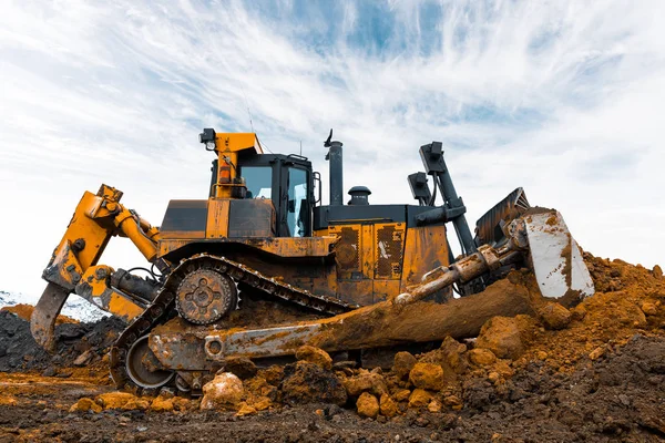 Žlutý bagr v kariéře přesune skrývky. Buldozer hřebeny na zem, s jasné slunce a pěkné modré obloze na pozadí — Stock fotografie