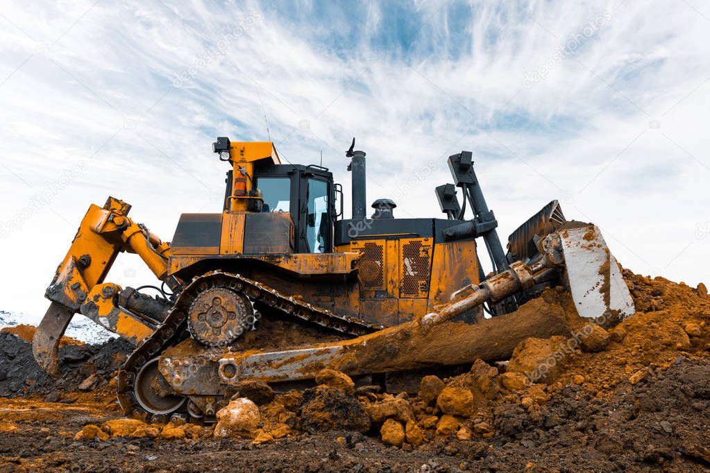 Yellow excavator in career moves overburden. Bulldozer combs the ground, with the bright sun and nice blue sky in the background