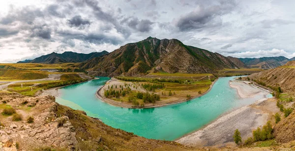 Panorama of mountain river on background of beautiful mountains in cloudy weather. View of turquoise river in the mountains on the background gloomy sky